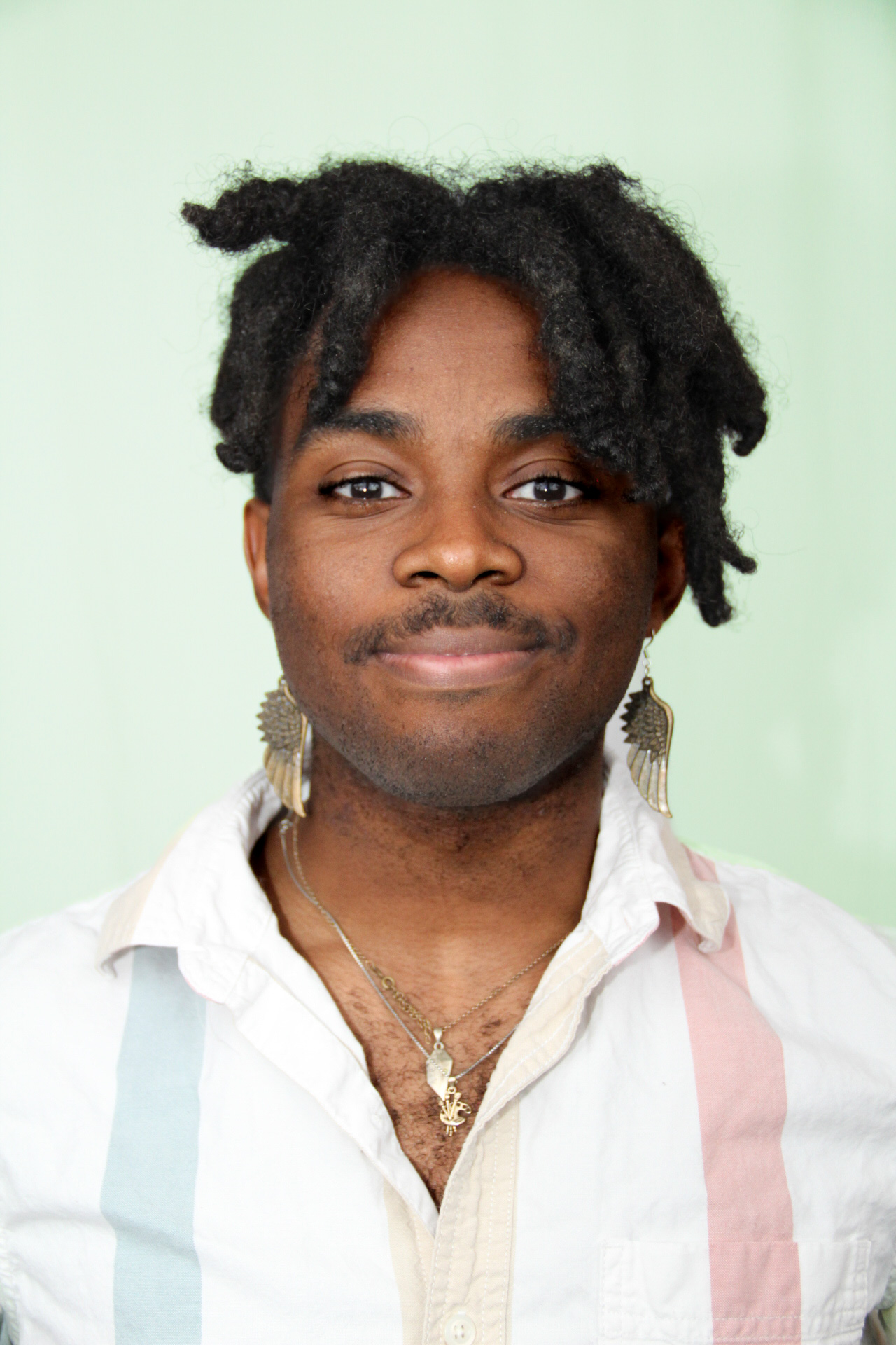 A person with dreadlocks wearing a white shirt and a pink and white striped shirt  AI-generated content may be incorrect.